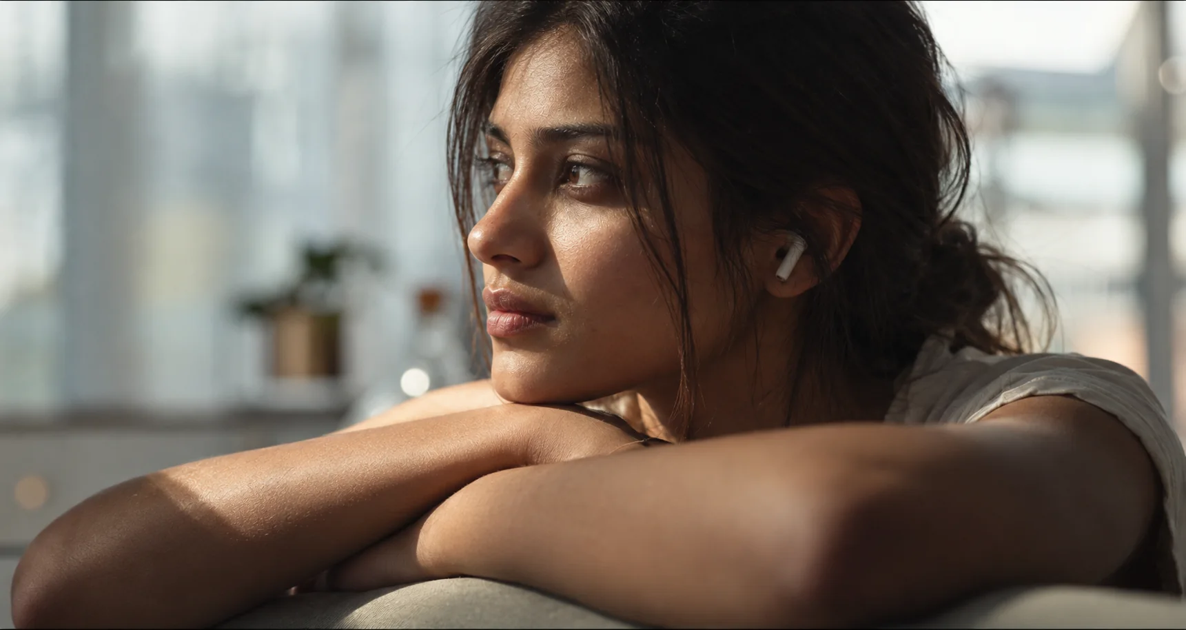 A woman wearing an earbud rests beside a sunlit window