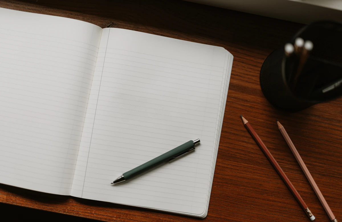An open notebook with a pen on a wooden desk